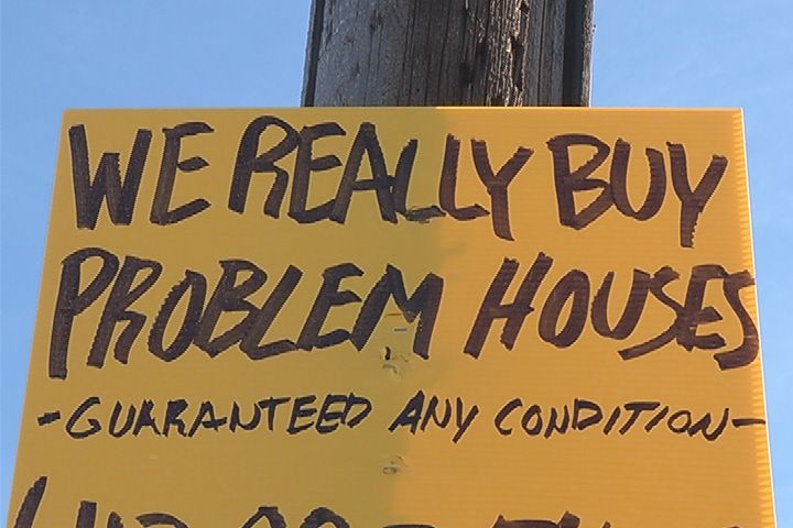a yellow we buy houses sign stapled to a telephone pole.